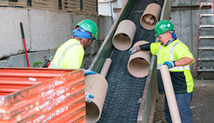 Two Casella workers working with recycling waste on a conveyor belt.