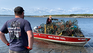 One person standing at the end of the lake while another person in a boat filled with trash pulls up.