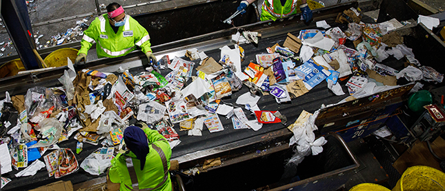 Two Casella workers sorting recycling waste on a conveyor belt.