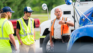 Three workers standing and talking in a parking lot of trucks.