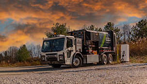 A Casella waste truck parked in front of a forest charging. 