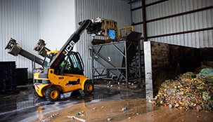 A small yellow forklift loads recycle  materials into a hopper in an recycle facility