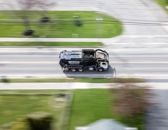 An aerial view of a Casella waste management truck driving down a suburban road.