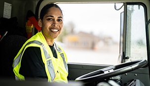 An employee sitting down in a tuck at the wheel smiling towards the passenger