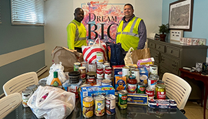 Two workers standing in an office with food donations on the table.