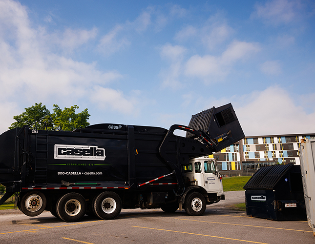 Casella waste truck picking up a Dumpster in a parking lot of an apartment complex