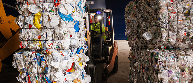 A worker operating a forklift moves large bales of compressed recyclable materials, in a recycling facility.